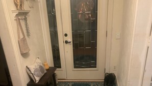 Un plancher en bois mène à une porte blanche dotée d’un panneau en verre. Un tapis bleu à motifs est placé devant la porte.
