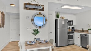 A modern kitchen with white cabinets, stainless steel appliances, and a wooden dining table with wicker chairs.