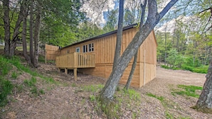 A wooden cabin with a balcony, surrounded by trees and a dirt path.