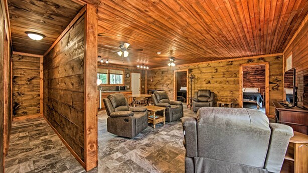 A log cabin interior with a wooden ceiling, a dining area with a table and chairs, and a living room with sofas and a fireplace.