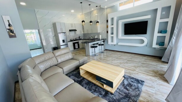 A modern living room with a beige sectional sofa, a wooden coffee table, and a kitchen area in the background.