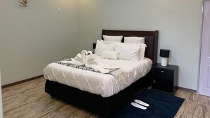 A neatly made bed with a dark headboard, a bedside table with a lamp, and a blue rug on the floor.