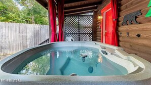 Un bain à remous dans un chalet en bois, entouré d’une clôture en bois et doté d’une porte rouge.