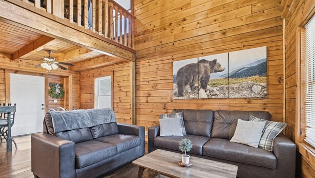 L’intérieur d’un chalet en bois, avec deux canapés en cuir, une table basse en bois et un ventilateur de plafond.