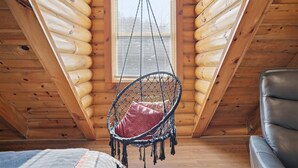 L’intérieur d’un chalet en bois, avec un fauteuil suspendu, une fenêtre et un canapé.