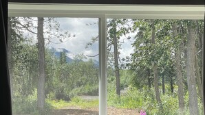 A room with a large window overlooking a forested area with trees and a mountain in the distance.