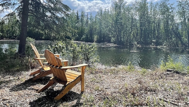 A wooden chair by a lake surrounded by trees.