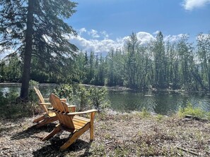 A wooden chair by a lake surrounded by trees. - Modern Rustic Cabin with Denali View (Cantwell)