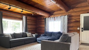 A cozy log cabin interior with a grey sofa, a blue sofa, and a patterned rug.