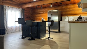 A modern kitchen with wooden walls, a stainless steel refrigerator, a coffee maker, and two bar stools.