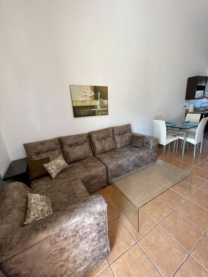 A living room with a brown sectional sofa, a glass coffee table, and a dining area with a white table and chairs. - Beautiful Coco Beach 2 Bedroom Condo (playas del coco)