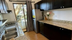 Una cocina con armarios oscuros, encimera de granito, pileta de acero inoxidable y refrigerador.