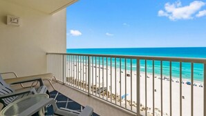 A balcony with a view of a beach, a table, and chairs.