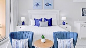 A hotel room with a large bed, two nightstands, a round wooden table, two blue armchairs, and artwork on the walls.