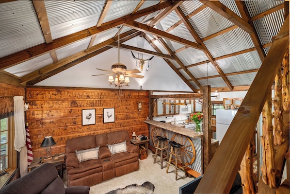 A rustic cabin interior with a wooden ceiling, a dining area with a bar, and a cozy living space with a sofa and a fireplace.