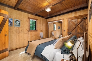 A rustic wooden room with a bed, a small window, and a door.