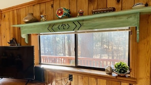 Habitación con paneles de madera, un televisor sobre una mesa de madera, una ventana con barandilla roja y una estantería con objetos decorativos.