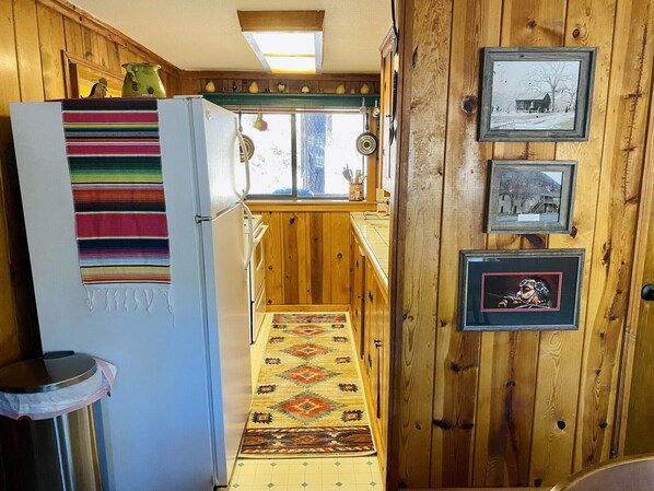 A narrow hallway with wooden walls, a refrigerator with a colorful striped towel, a patterned rug, and framed pictures on the wall. - 3 Little Bears - GREAT location; secluded feel! (Ruidoso)