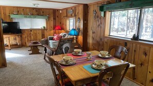Interior acogedor de una cabaña con una mesa de madera dispuesta para tomar té, rodeada de sillas de madera.