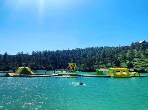Ein See mit schwimmenden Strukturen und eine bewaldete Hügelkette im Hintergrund.