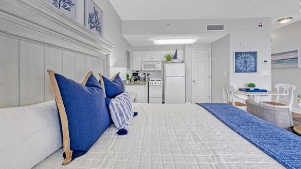 A modern bedroom with a large bed, a small kitchenette, and a dining area.