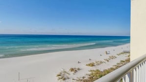 Vista de la playa desde un balcón, con cielo despejado, arena y algunas personas a lo lejos.
