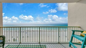A balcony with a view of a beach, a chair, and a small table. - BeachFront - Ocean View- Majestic Beach Resort 709 (Panama City Beach)