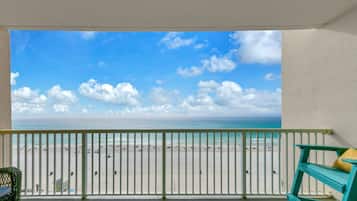 Een balkon met uitzicht op een strand, een stoel en een klein tafeltje.