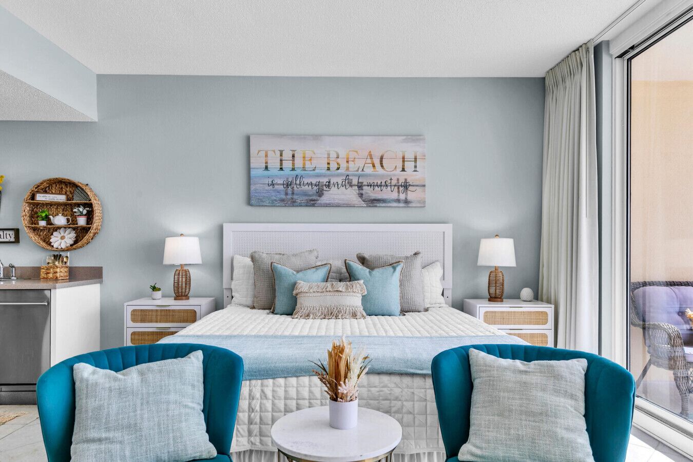 Een moderne slaapkamer met een groot bed, twee nachtkastjes, een bijzettafeltje en uitzicht op het strand door het raam.