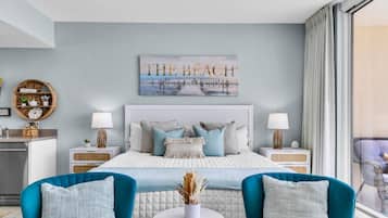 Een moderne slaapkamer met een groot bed, twee nachtkastjes, een bijzettafeltje en uitzicht op het strand door het raam.