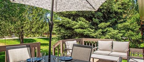 Une terrasse extérieure avec une table dressée pour le repas, entourée de meubles en bois et d’un grand parasol à motifs.