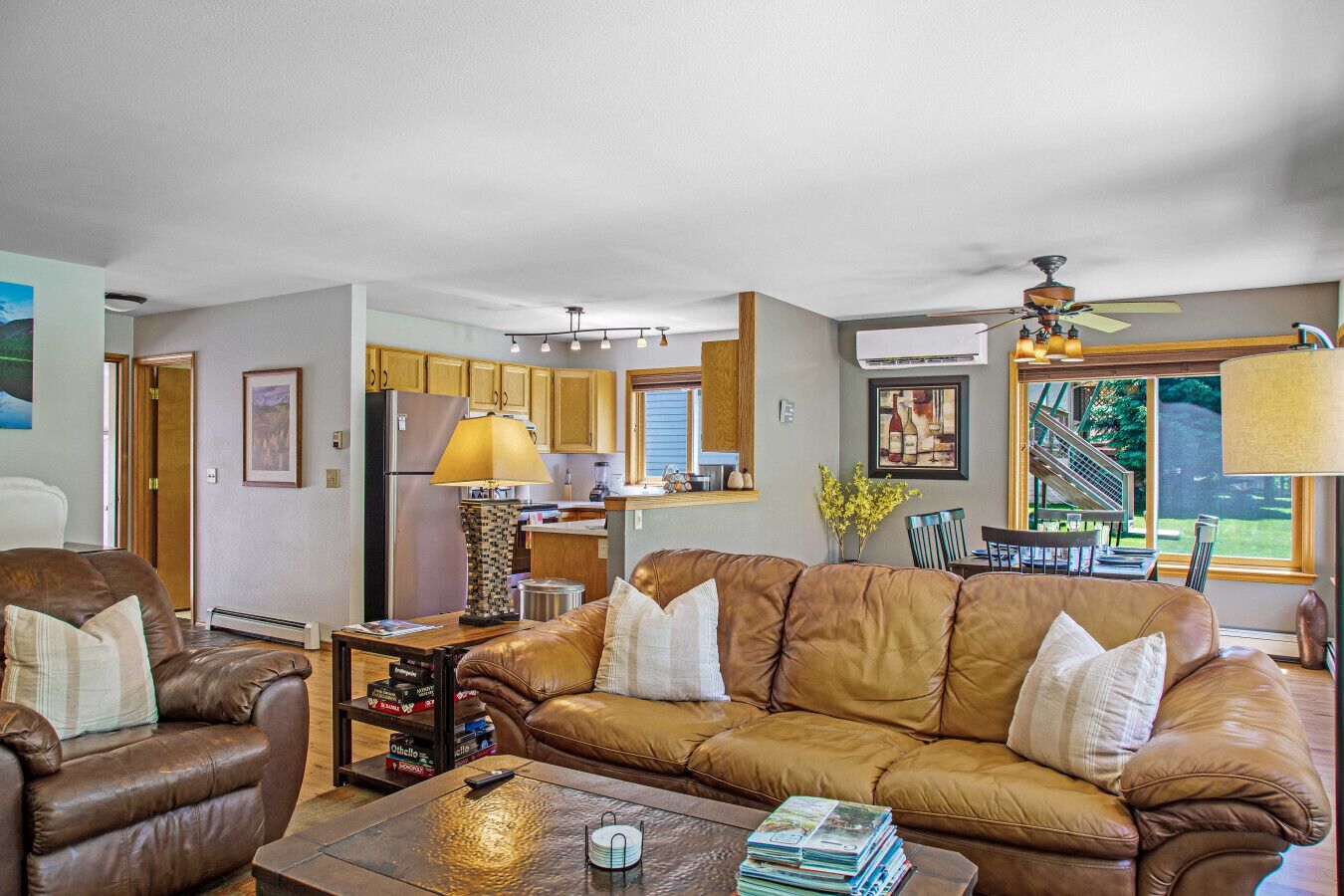 A spacious living room with a brown leather sofa, a coffee table, and a fireplace. There is a kitchen area with wooden cabinets and a dining area with a table and chairs.