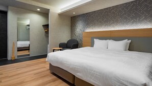Ett modernt hotellrum med en stor säng, en sänggavel i trä, en liten sittgrupp och en spegel som reflekterar badrummet.