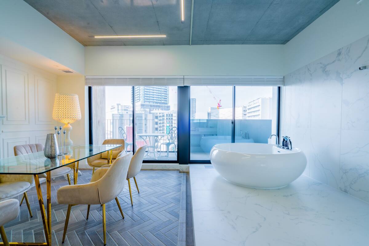 A modern bathroom with a large bathtub, a glass table with chairs, and a view of the city through large windows.