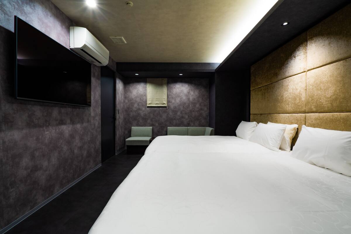 A modern hotel room with a large bed, a flat-screen TV mounted on the wall, a seating area with two chairs, and a small window.