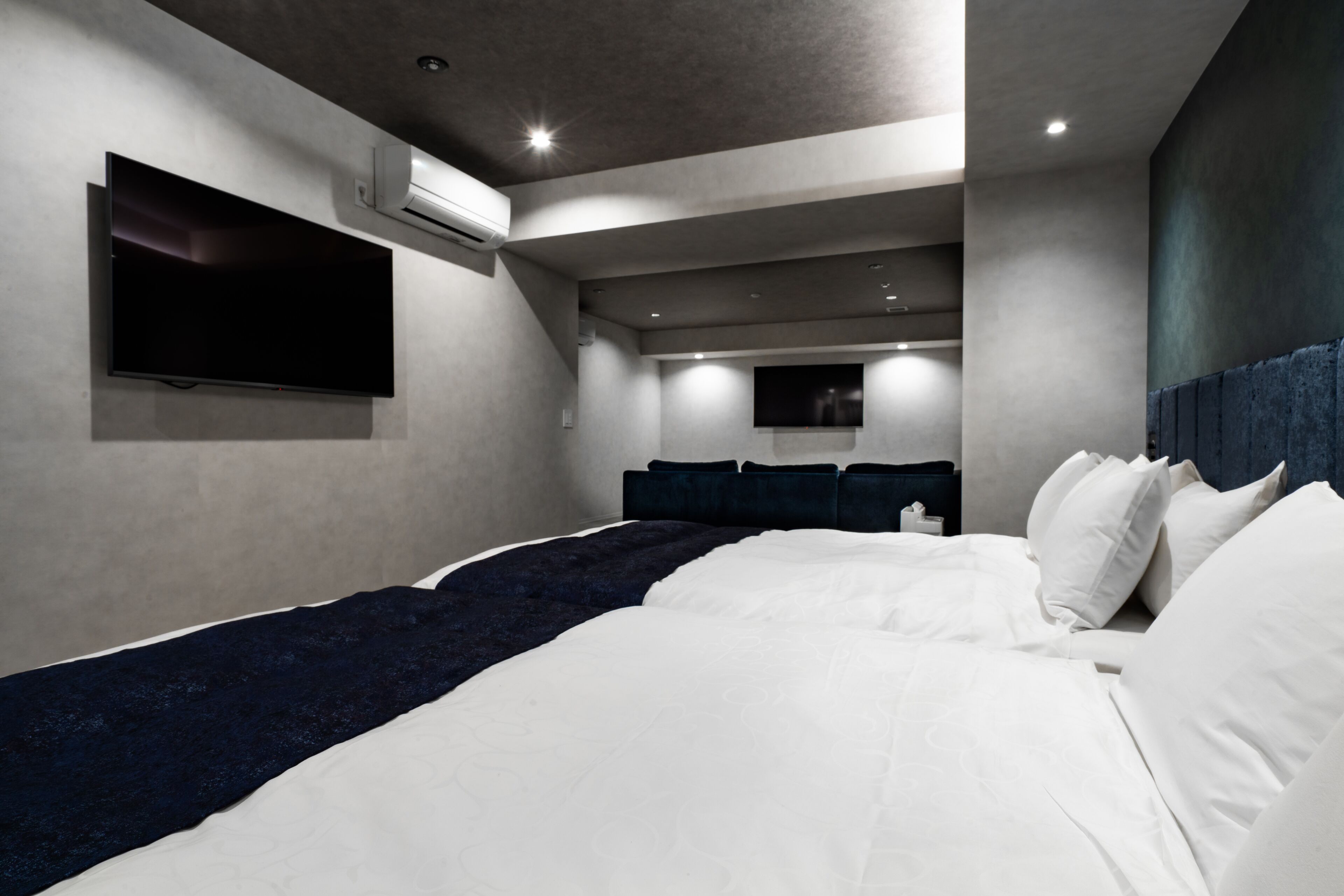 A modern hotel room with a large bed, a flat-screen TV mounted on the wall, and a ceiling-mounted air conditioning unit.