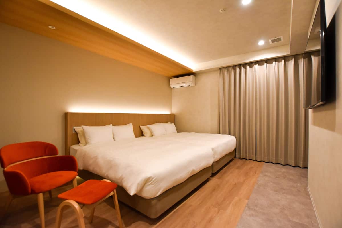 A modern hotel room with a wooden ceiling, a large bed with white bedding, a red chair, and a flat-screen TV mounted on the wall.