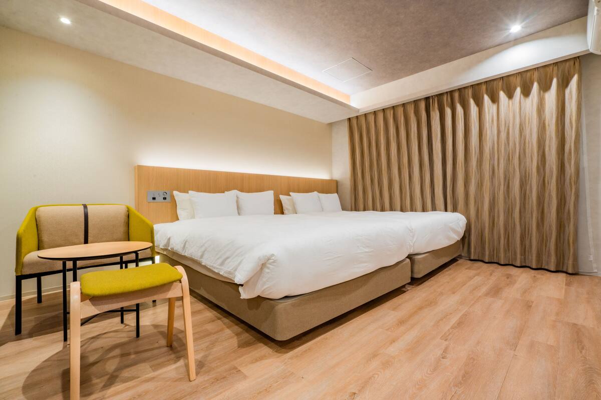 A hotel room with a bed, a chair, a small table, and a curtain.