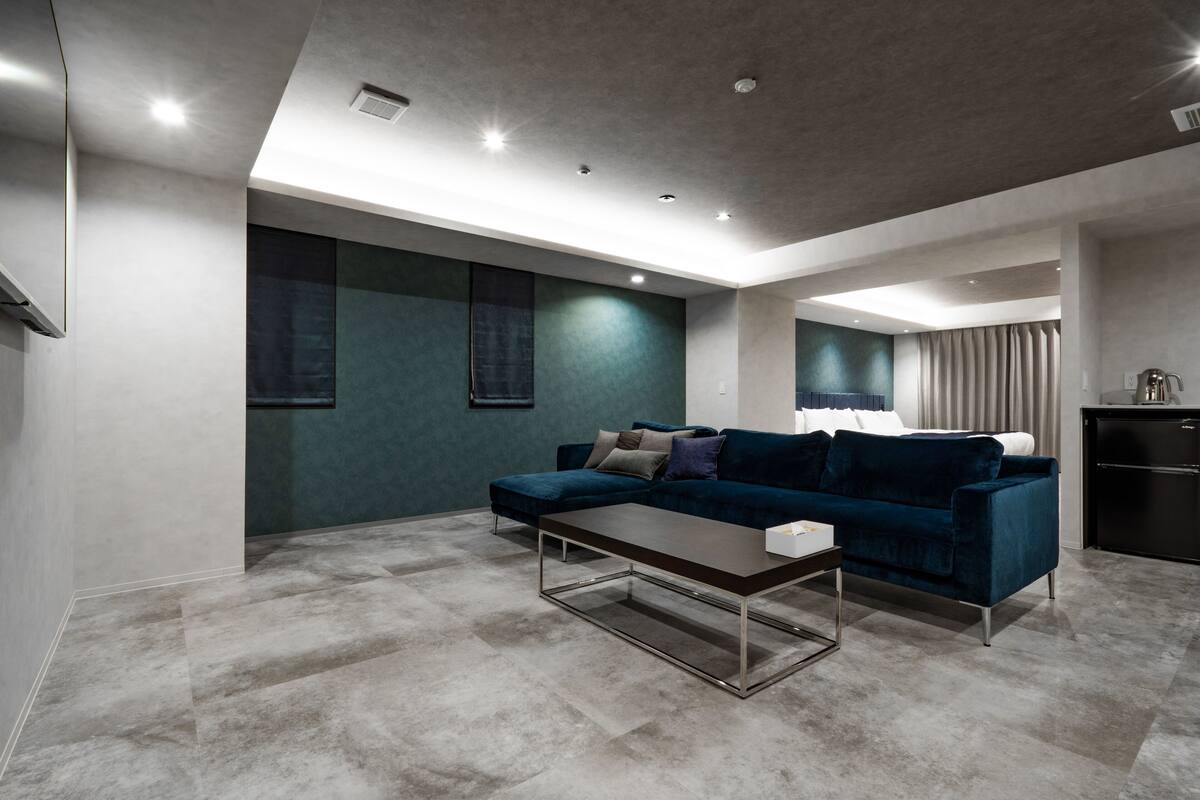 A modern living room with a dark blue sofa, a coffee table, and a kitchen area in the background.