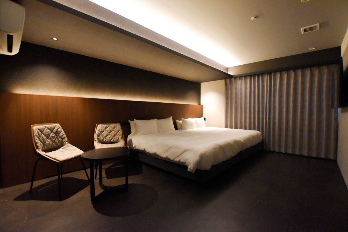 A hotel room with a large bed, two upholstered chairs, a small table, and a large window with curtains.