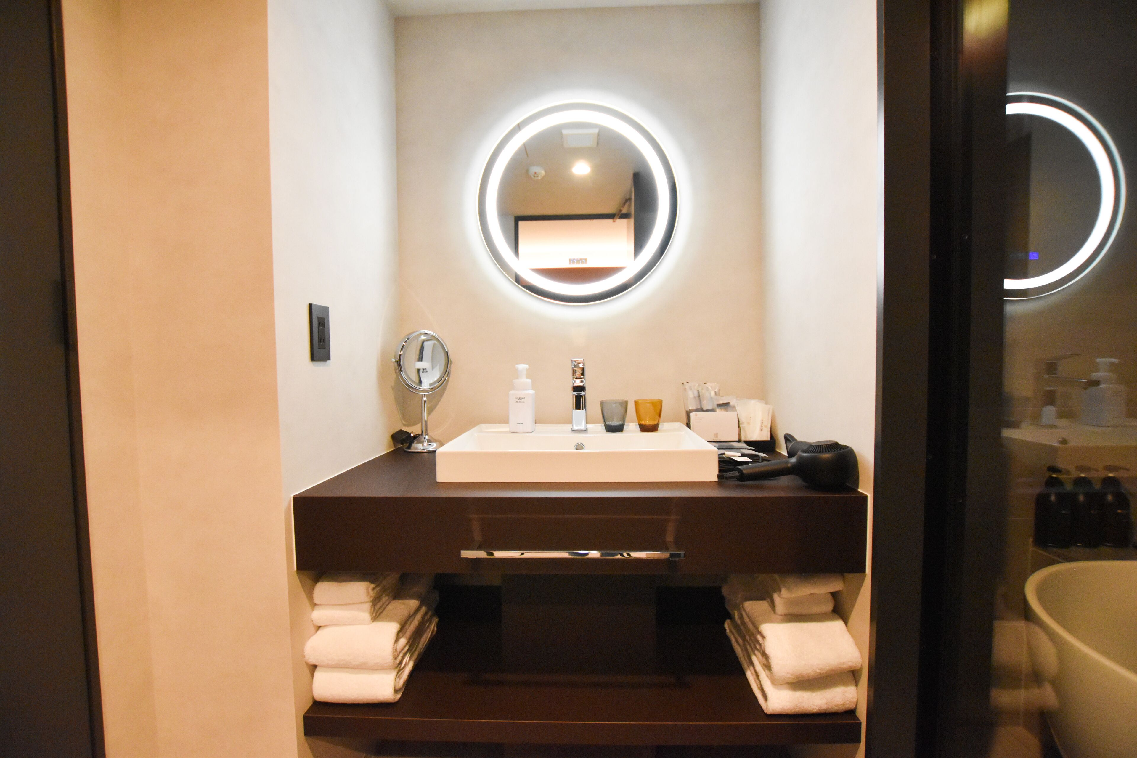 Een moderne badkamer met een grote spiegel, een wastafel en een bad. Er liggen handdoeken en toiletartikelen op het aanrecht.