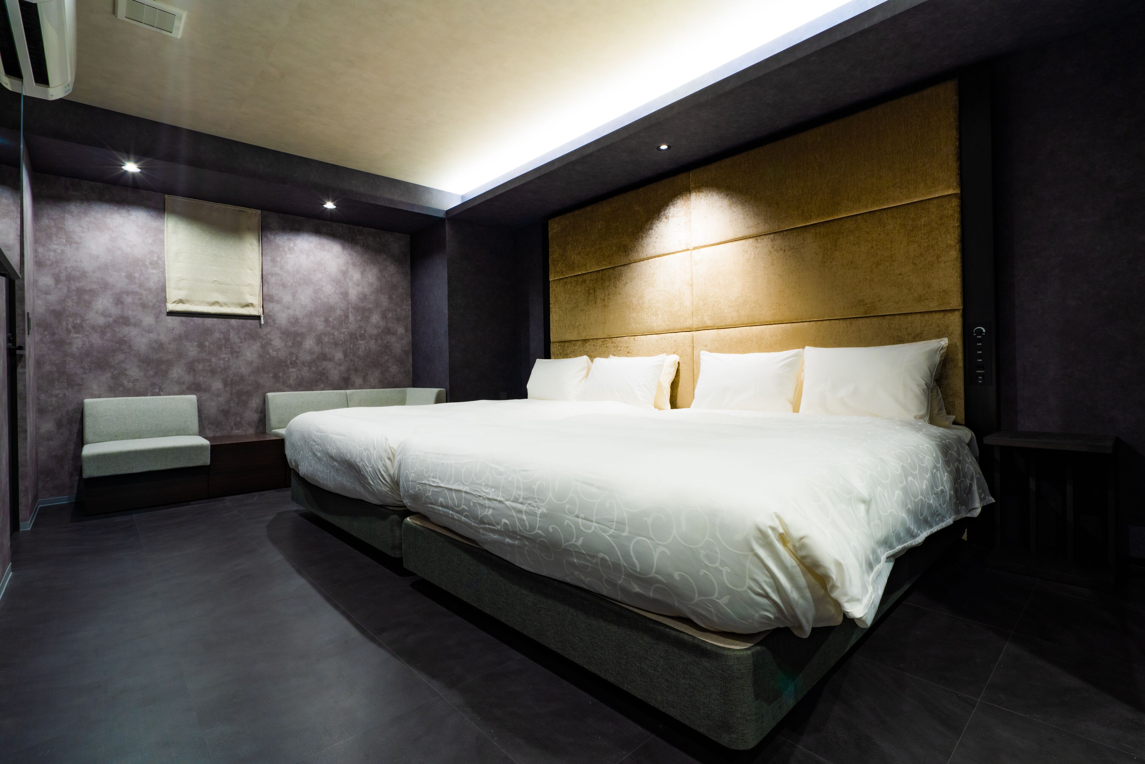 A modern bedroom with a large bed, a bench, and a headboard with built-in lighting.