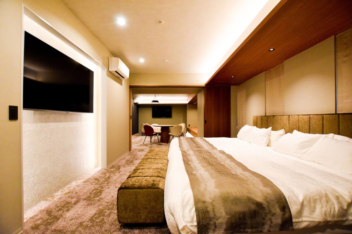 A hotel room with a large bed, a seating area with a table and chairs, and a television.