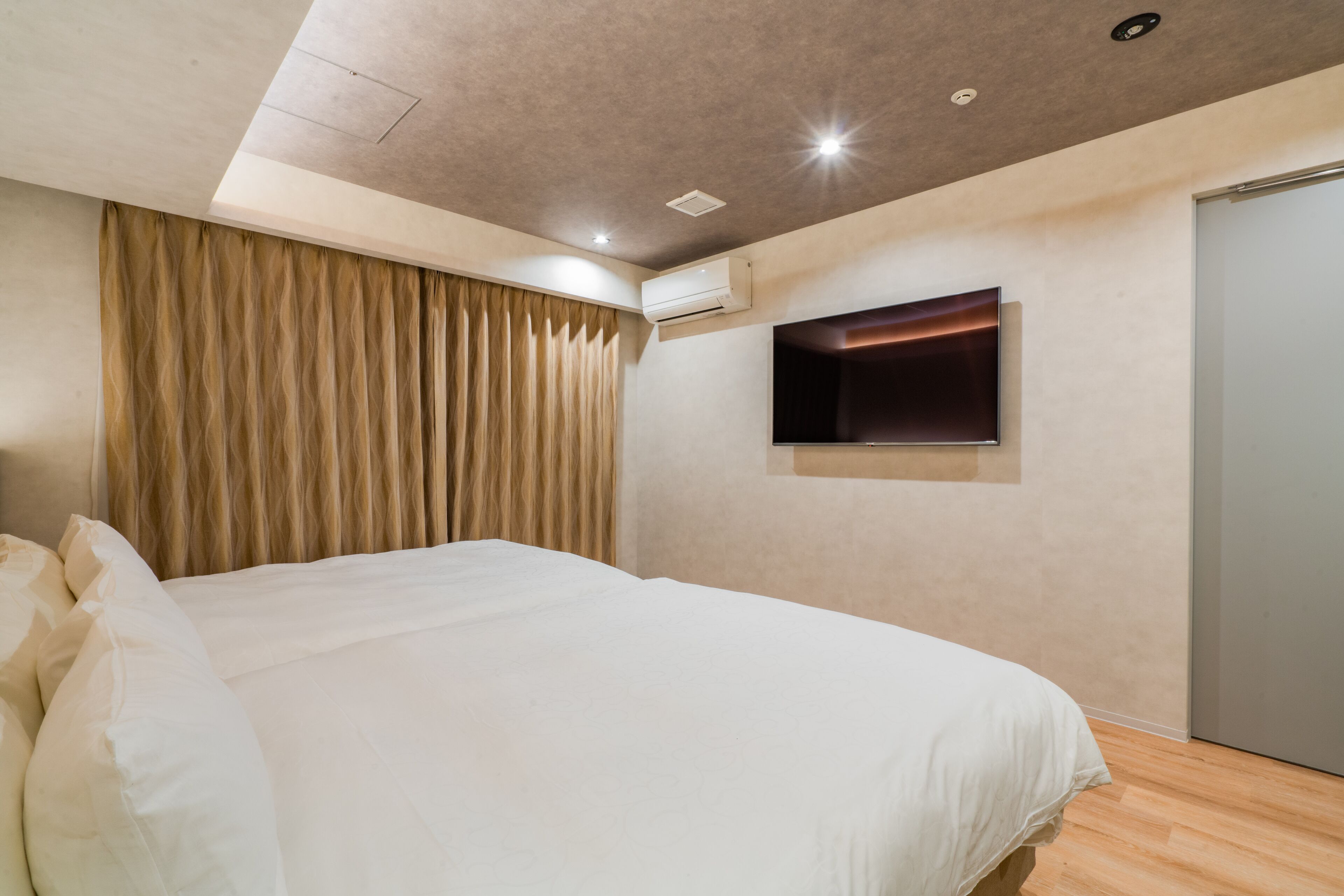 Un dormitorio moderno con una cama grande, un televisor de pantalla plana en la pared y un equipo de aire acondicionado.