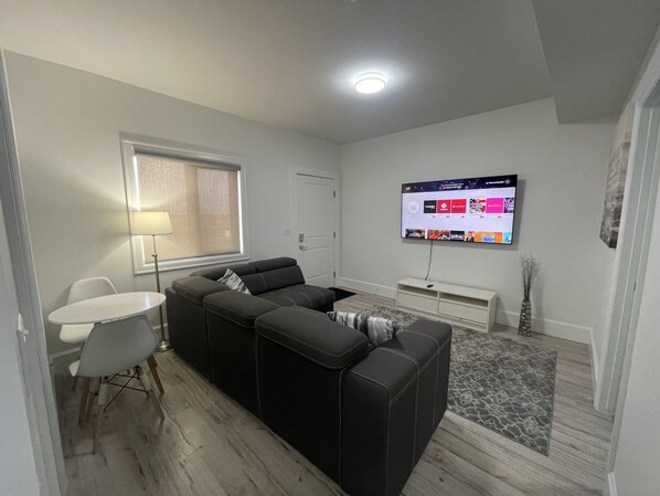 Un salon moderne avec un canapé d’angle, une petite table et un téléviseur à écran plat fixé au mur.