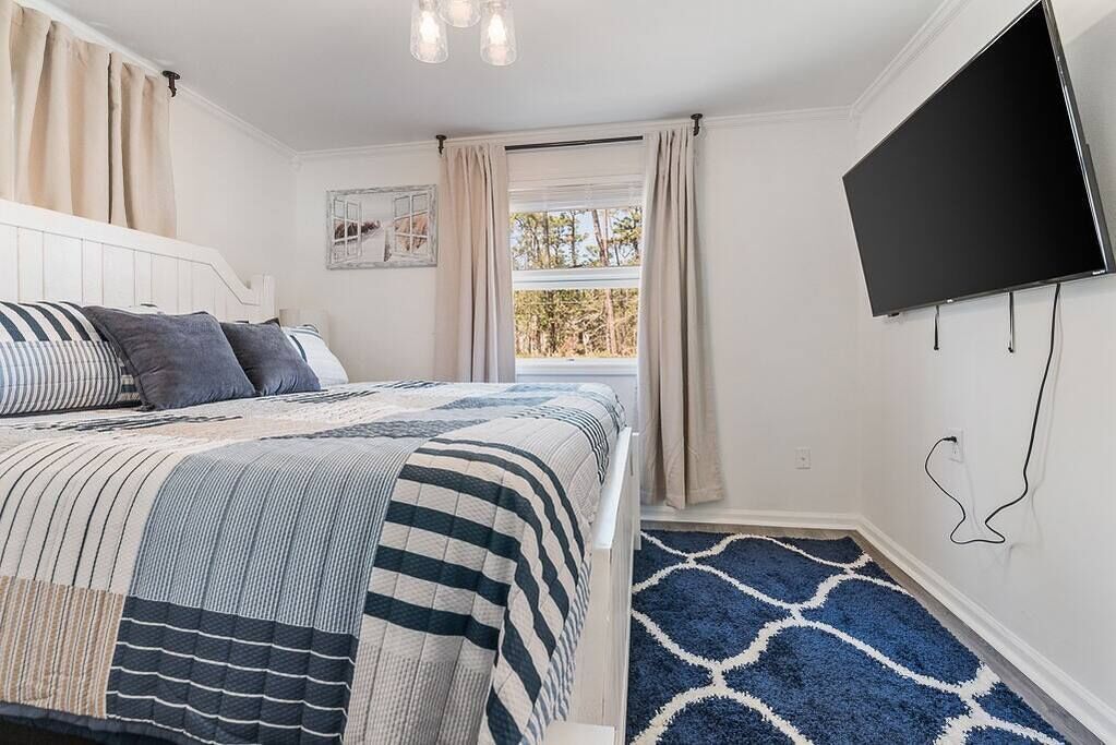 A bedroom with a bed, a TV, a window with curtains, and a patterned rug.