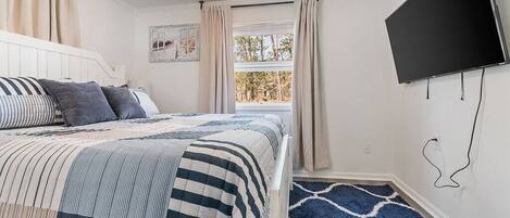 A bedroom with a bed, a TV, a window with curtains, and a patterned rug.