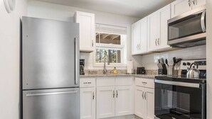 A modern kitchen with white cabinets, stainless steel appliances, and a window with blinds.