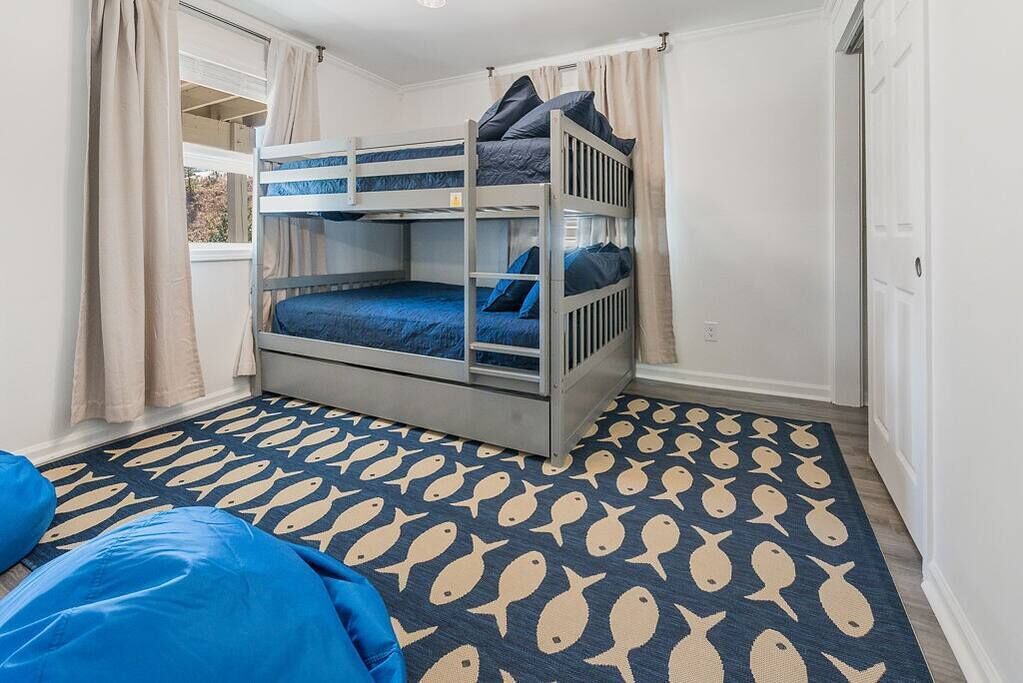 A bunk bed room with a patterned rug, a window with curtains, and a door.