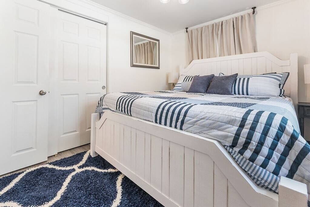 Un dormitorio con una cama blanca, ropa de cama a rayas, un espejo y una puerta.
